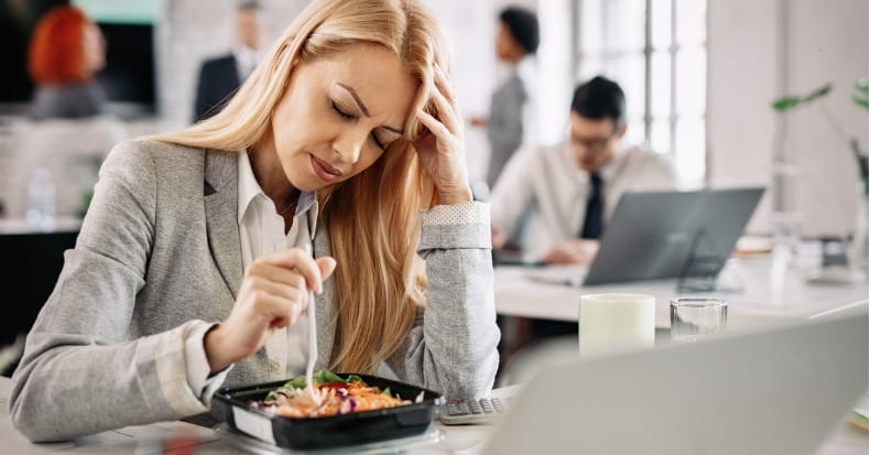 Businesswoman having headache while eating salad on lunch break