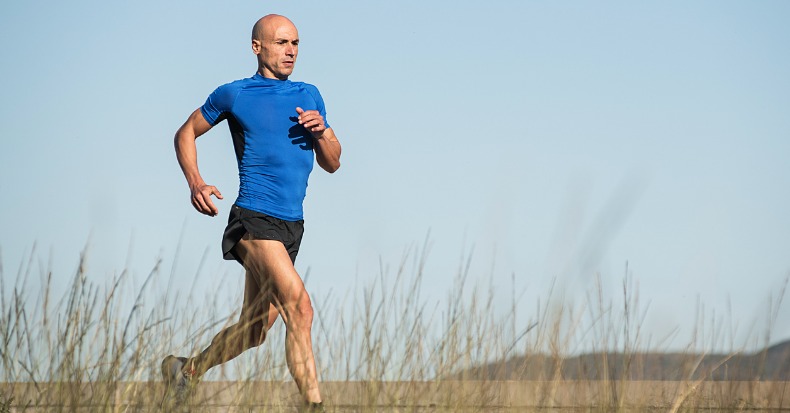 Adult male with shaved head and sportswear running along a grassy