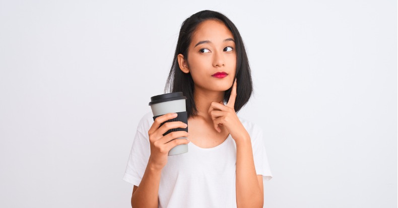 Young chinese woman drinking take away glass of coffee over isolated