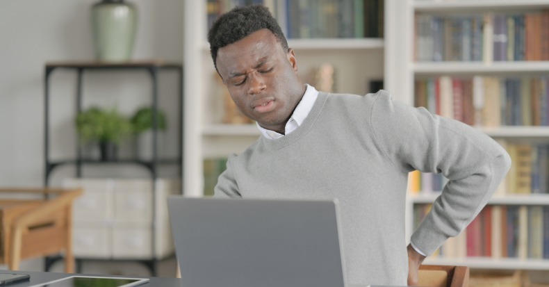 African man having back pain while using laptop in library